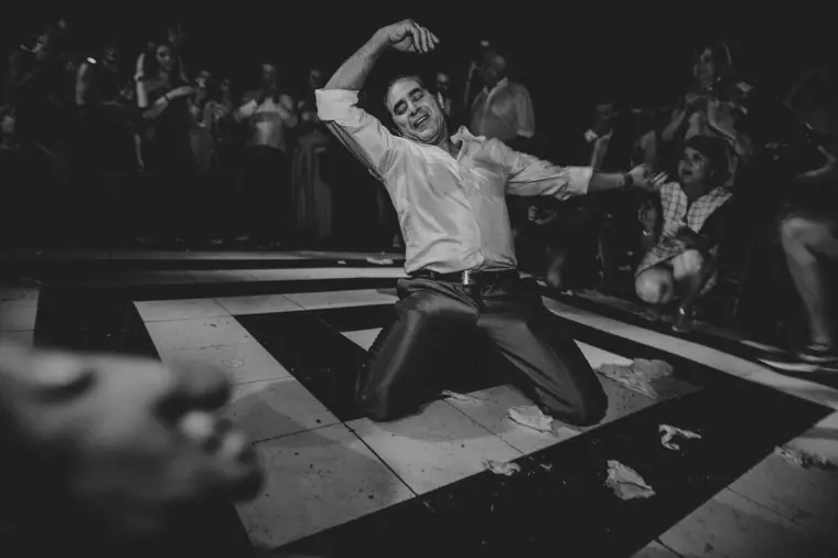 Black-and-white photo of a guest dancing on his knees on the dance floor