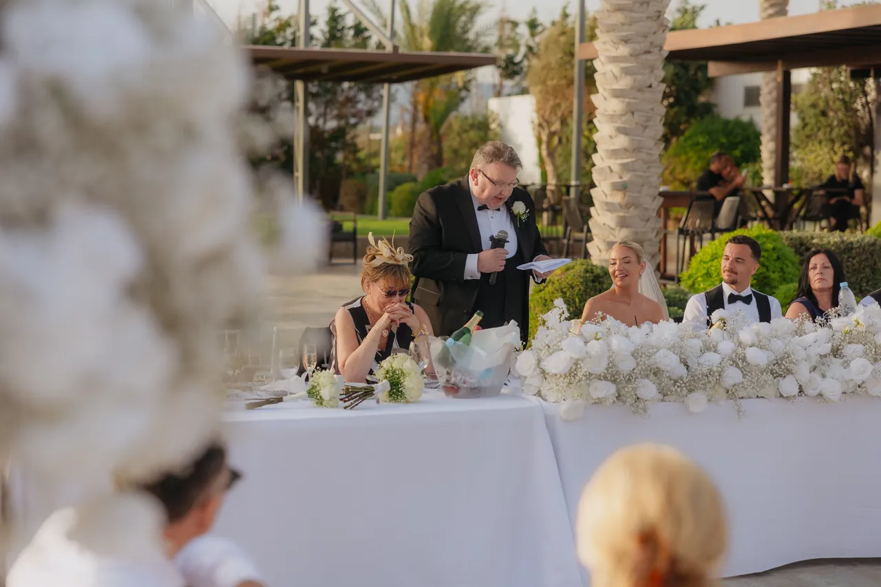 Guest giving a speech at the top table behind white flowers