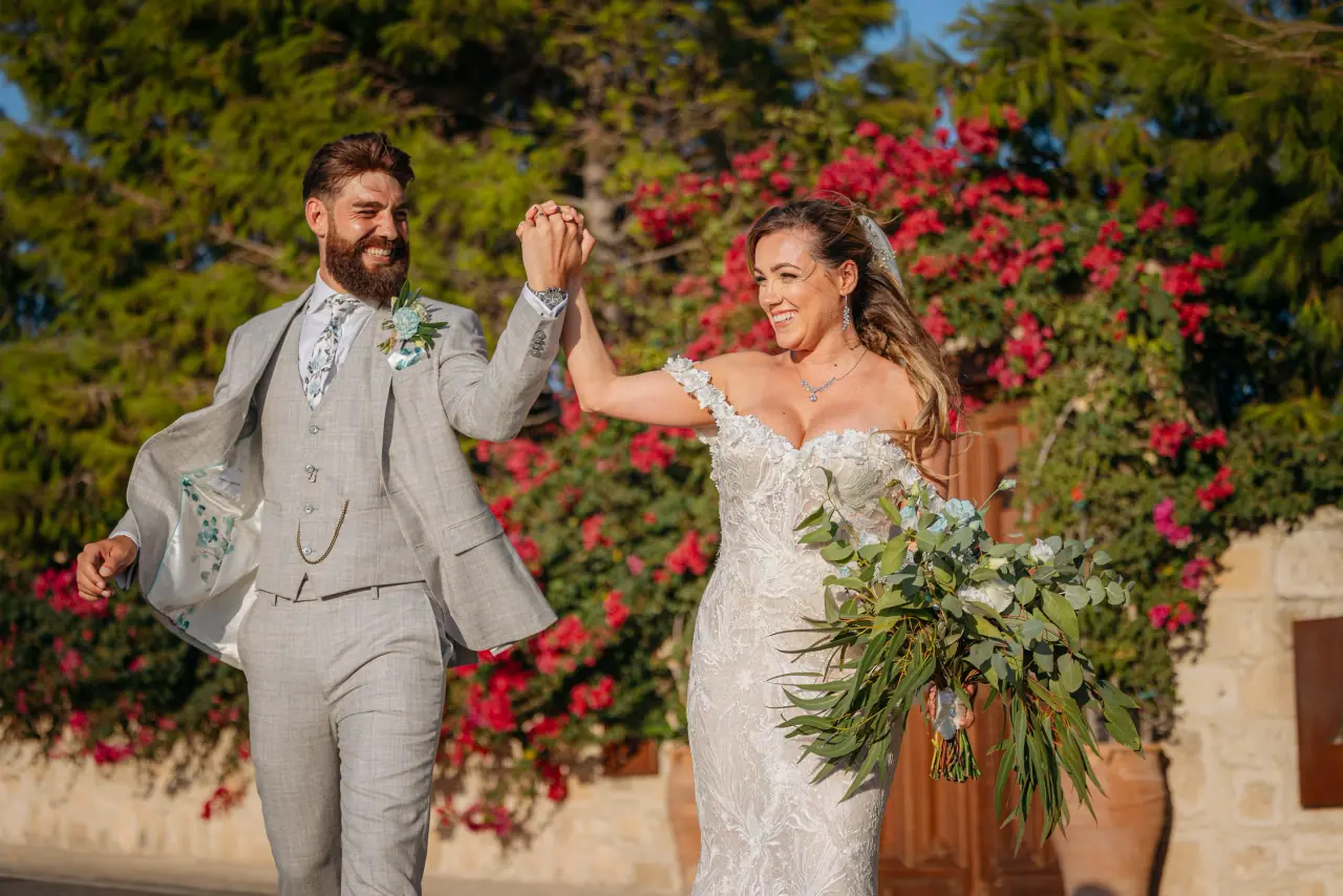 Annie and Iain dancing hand in hand before pink bougainvillea at Liopetro