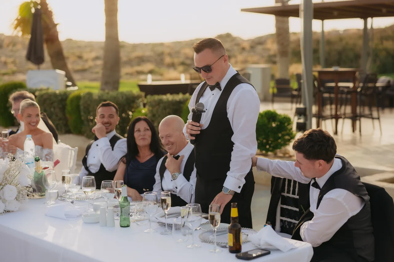 Groomsman in a waistcoat standing to give a speech at the top table