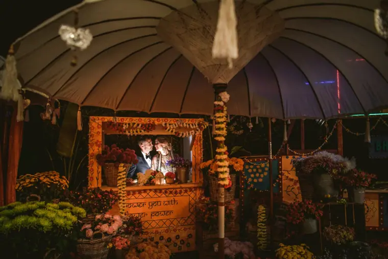 Couple seen through a lit window of a flower-decked kiosk under a large umbrella at night