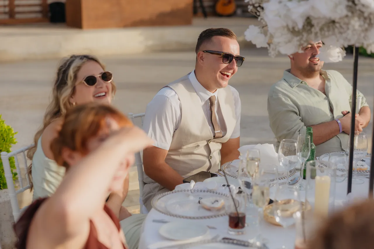 Guests in sunglasses laughing at their table during the speeches