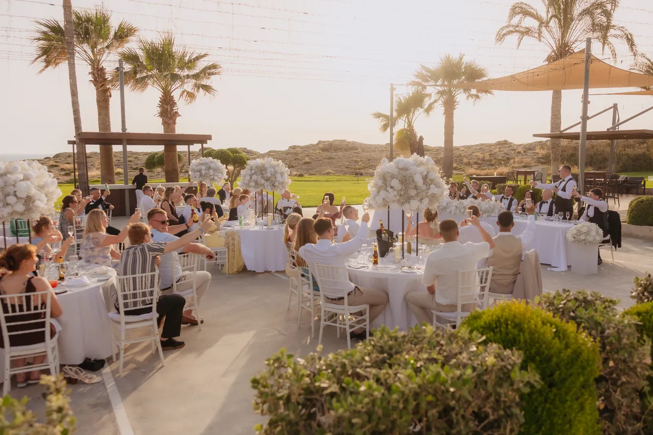 Wide view of the reception terrace with guests raising a toast at sunset