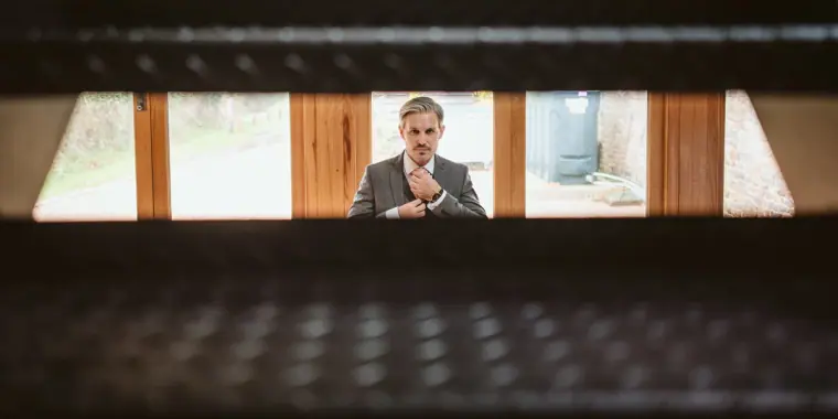 Groom adjusting his collar, framed through a narrow slatted gap