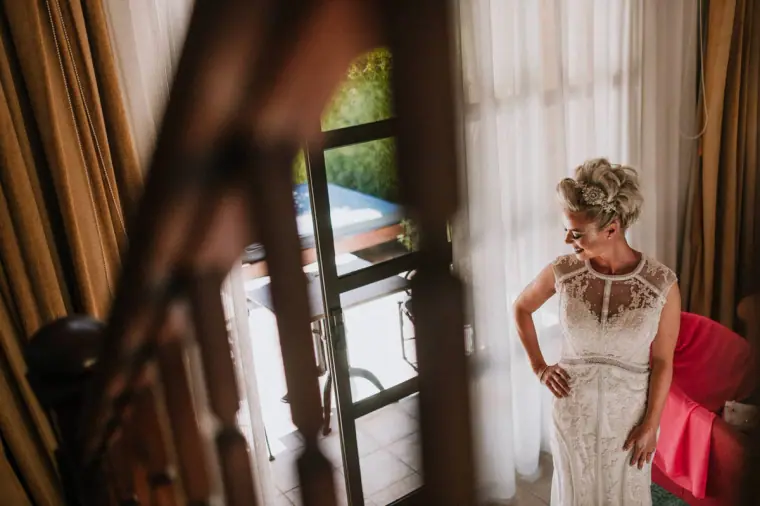 Woman in a beaded lace dress glancing down by a curtained window, Elysium, Paphos