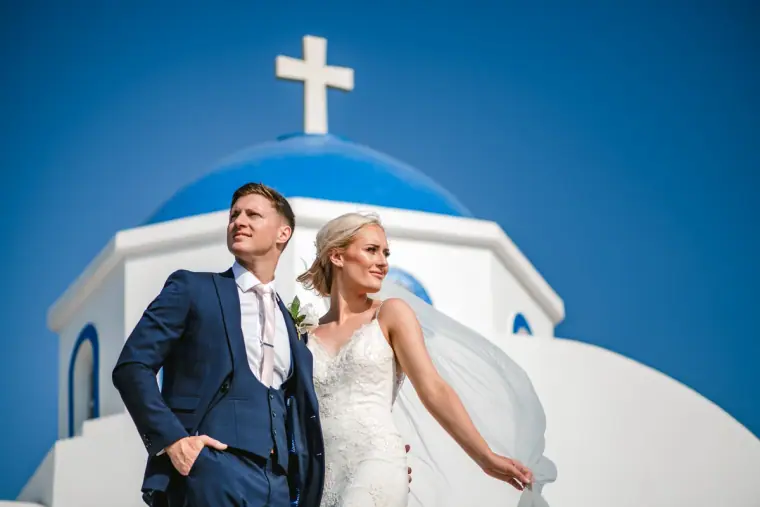 Couple posing in front of a blue-domed white chapel topped with a cross