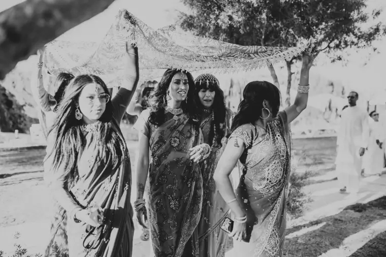 Black-and-white photo of women in saris dancing in procession beneath the canopy