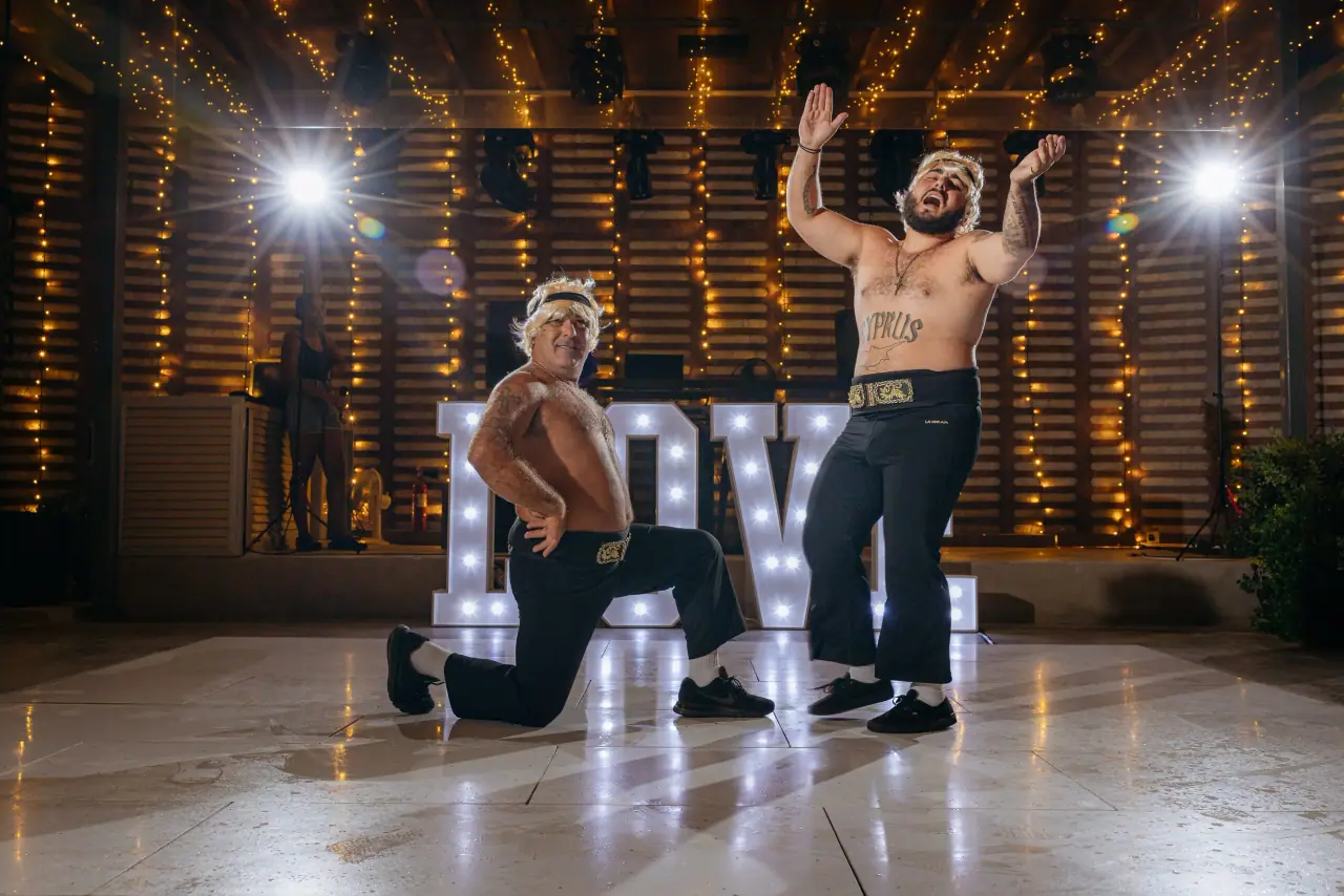 Shirtless guests posing in front of illuminated LOVE letters at Alassos