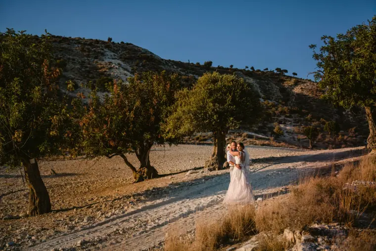 Bride and groom embracing on a dusty path among olive trees and rocky hills