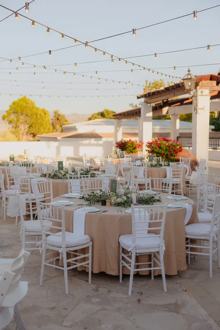 Round tables with white chairs and greenery beneath the pergola ahead of the reception