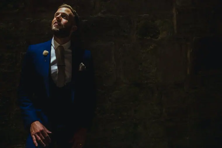 Groom in a navy suit gazing upwards in a dark, moody setting, Edinburgh