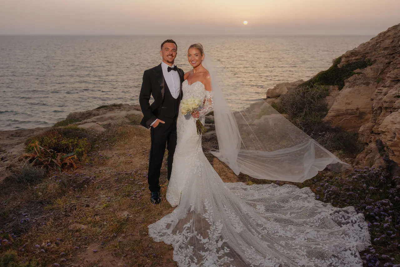 Olivia and Ashley smiling on the coast at sunset, her lace train spread out