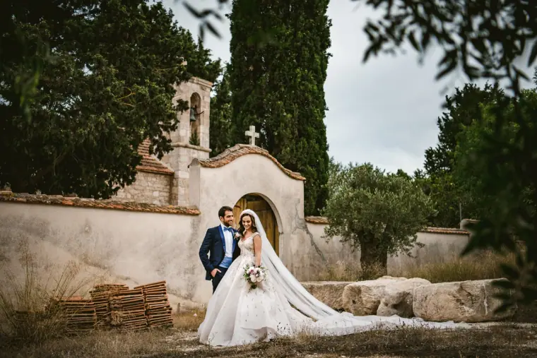 Bride and groom outside a small stone chapel with her long train fanned out