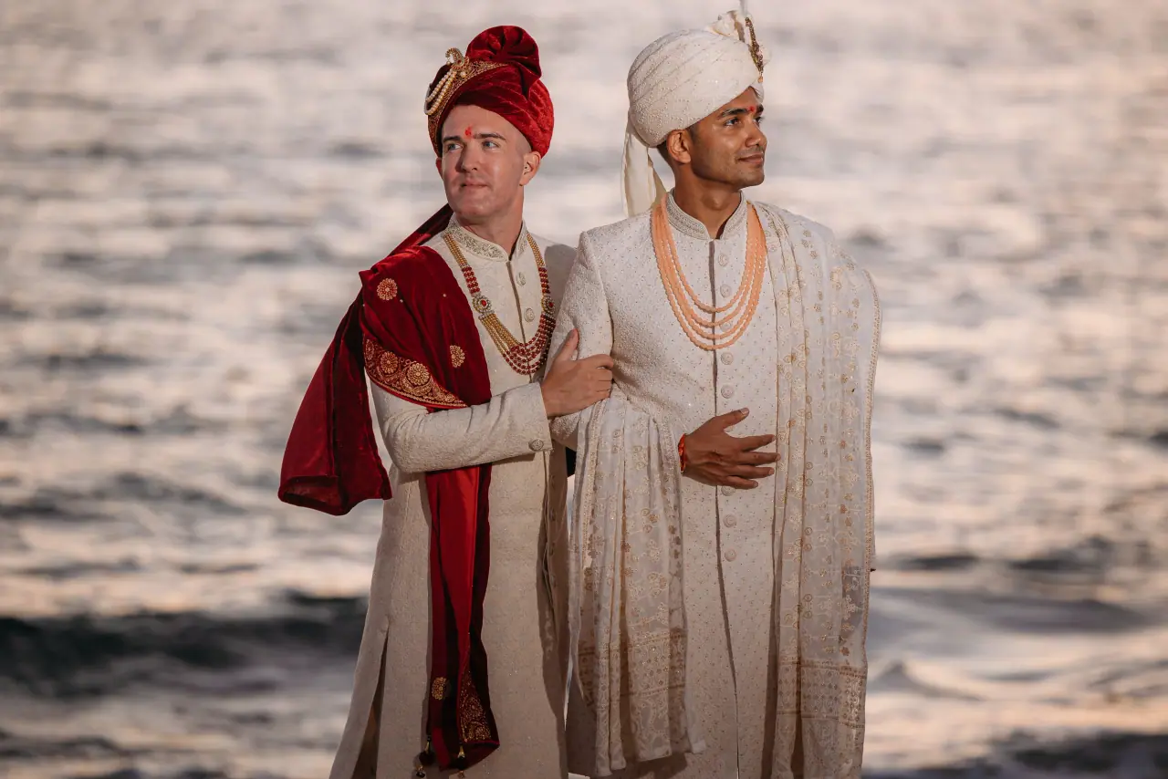 Daniel and Prashant arm in arm by the sea in traditional Indian wedding dress