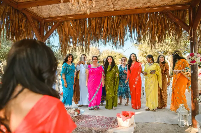 Procession arriving at the thatched beach canopy, seen past the bride's red sari
