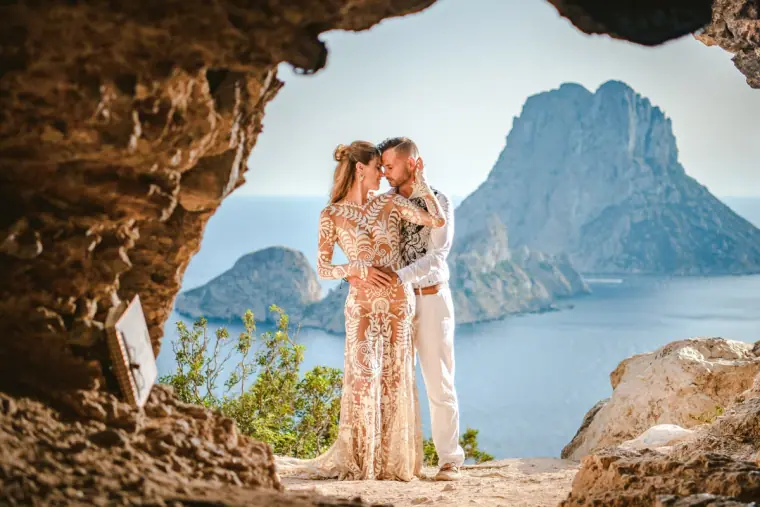 Couple embracing in a cave mouth overlooking a dramatic rocky island in a blue sea