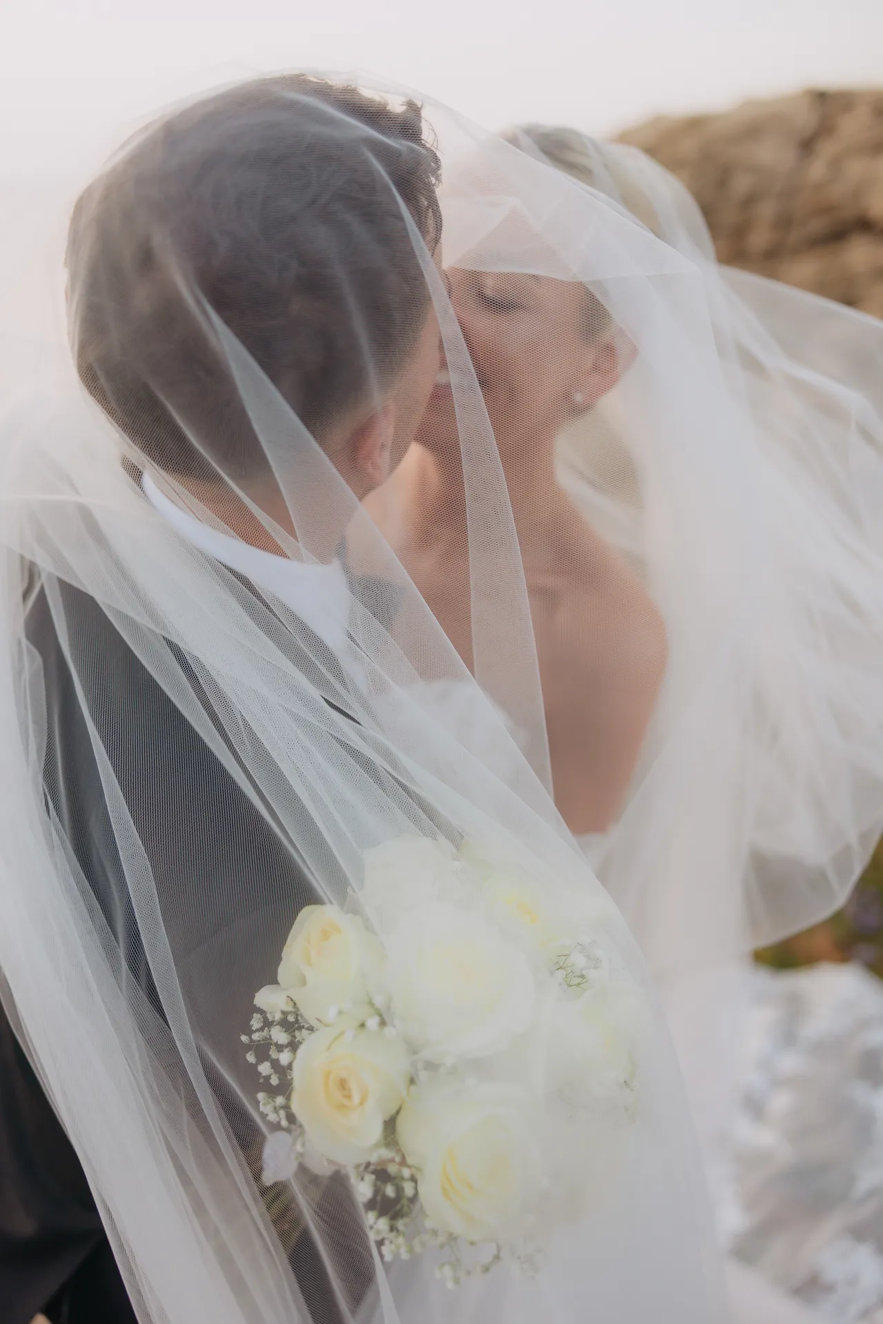 Bride and groom kissing under her windblown veil