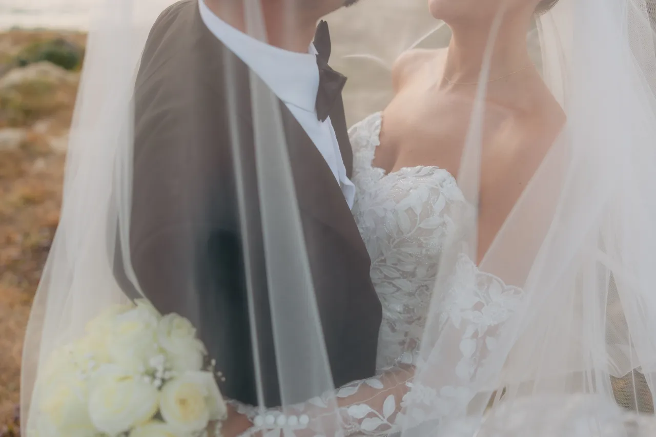Close-up of the couple wrapped in the veil with a bouquet of white roses