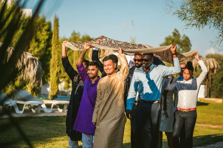 Groom's party carrying an embroidered canopy across the villa lawn