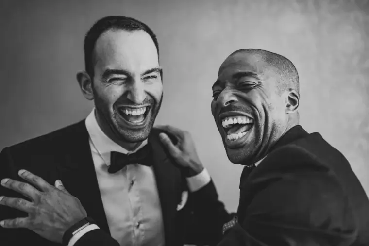 Black-and-white photo of two groomsmen in tuxedos laughing together