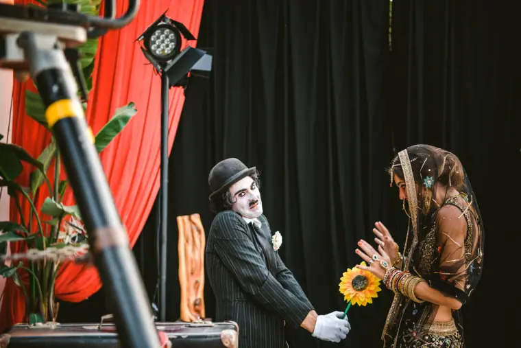 Chaplin-style entertainer offering a sunflower to a bride in an Indian headscarf on stage