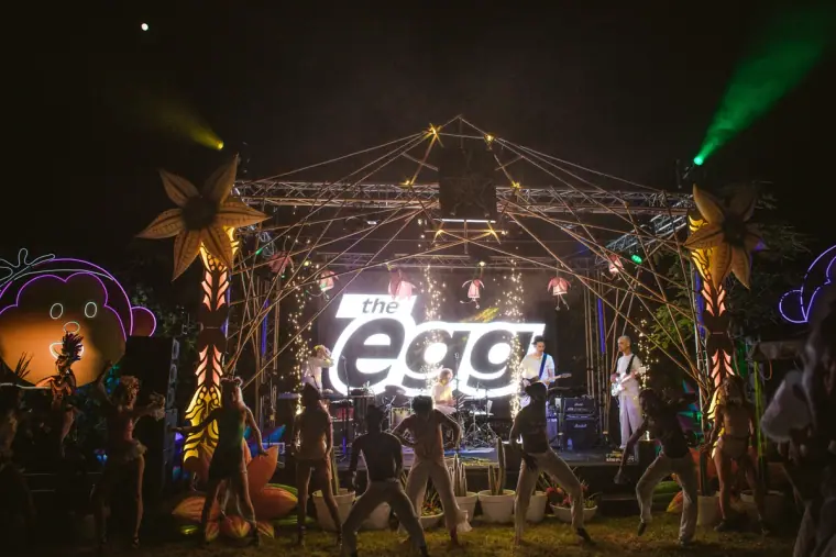 Guests dancing in front of a lit stage at a festival-style wedding party at night