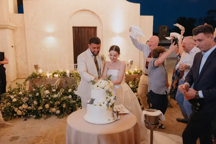 Poppy and Andrew cutting their cake as guests wave napkins