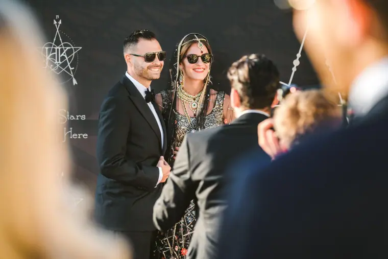 Bride in an Indian embroidered outfit and groom in sunglasses greeting guests