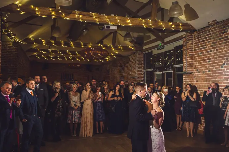 Guests watching the first dance beneath fairy-lit beams at Wasing Park