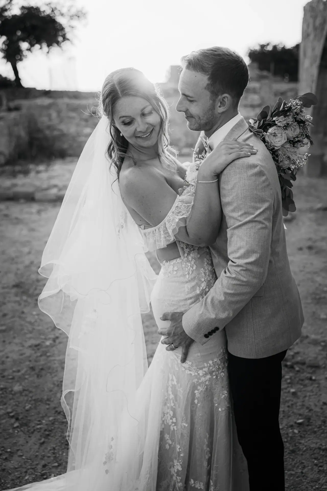 Black-and-white photo of Laura and Lewis embracing and laughing, groom holding the bouquet