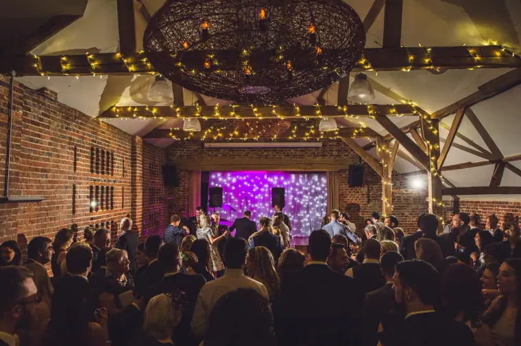 Packed dance floor beneath a large chandelier and fairy-lit beams, Wasing Park