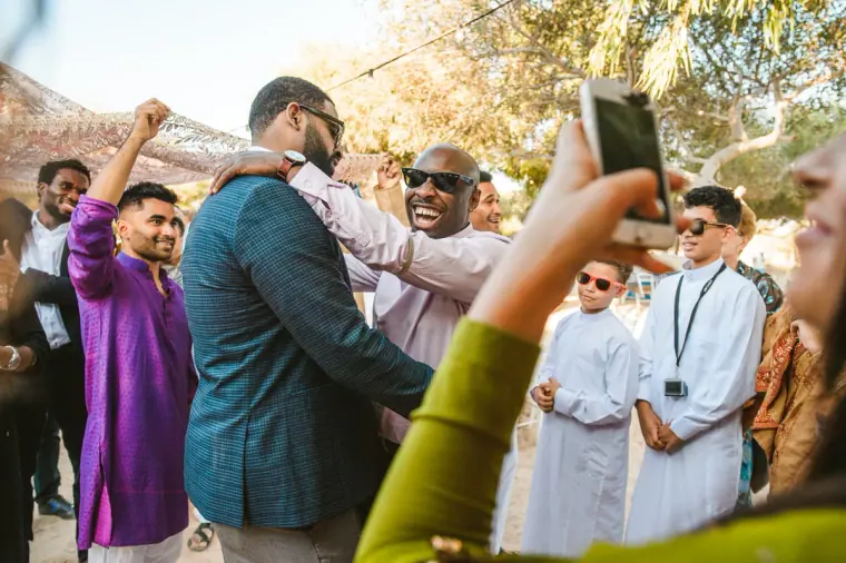 Groom's procession arriving as guests film on their phones beneath the trees