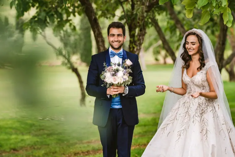 Groom holding a bouquet and smiling bride in a sparkling gown in an orchard