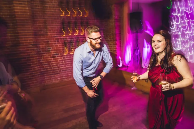 Guests dancing under pink lights against the brick barn wall
