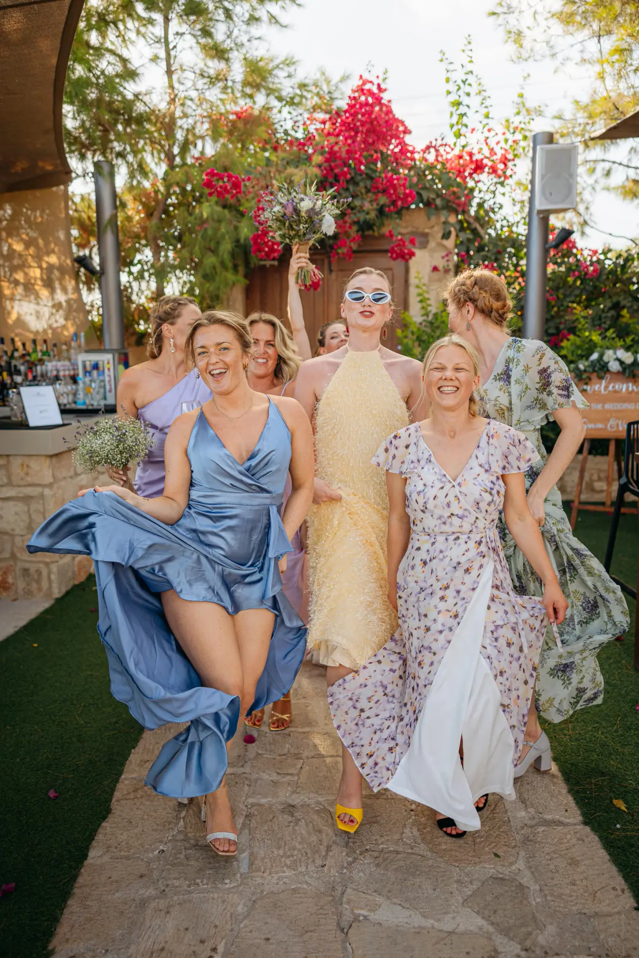 Vanja and her bridesmaids in colourful dresses walking beneath bougainvillea