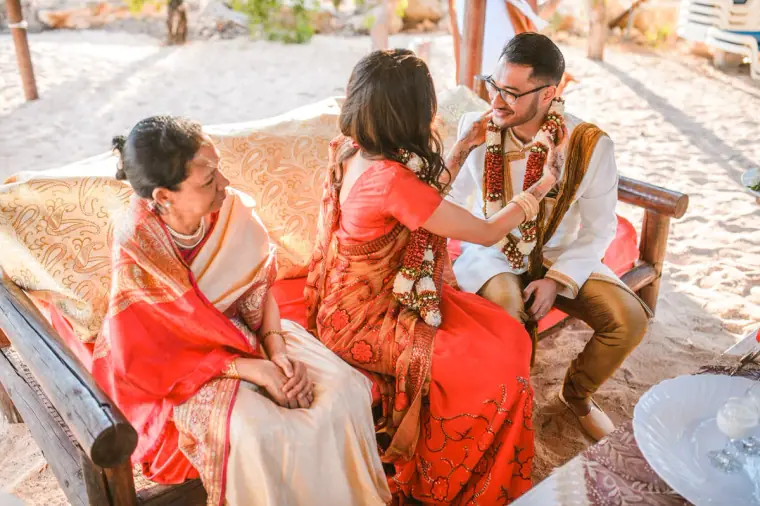Woman in a red sari adjusting the bride's garland as the groom watches