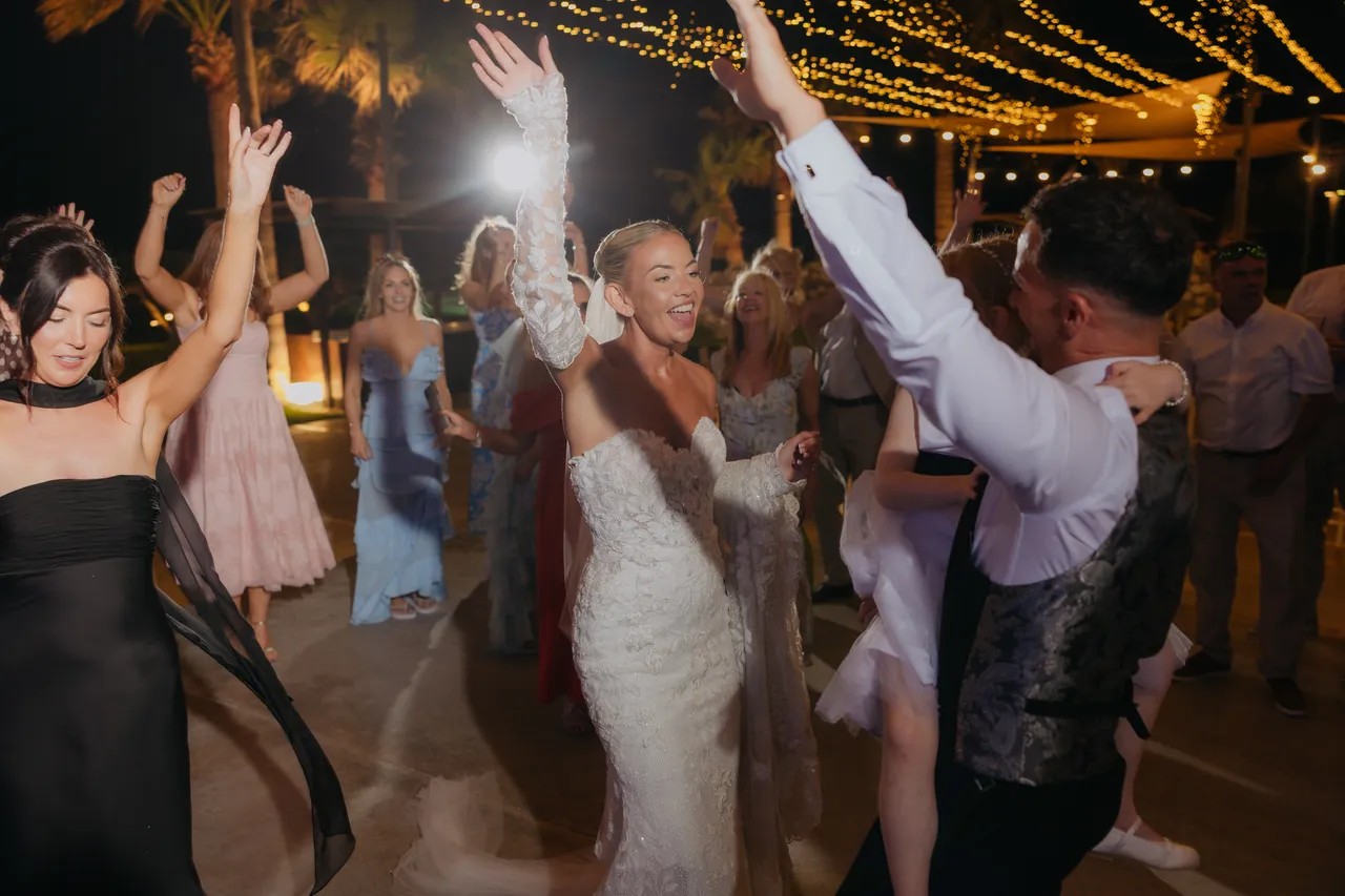 Bride and guests dancing with hands in the air under fairy lights