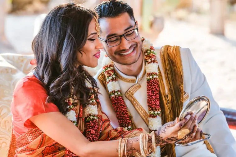 Raya and Adhib wearing flower garlands, laughing as they look into a mirror