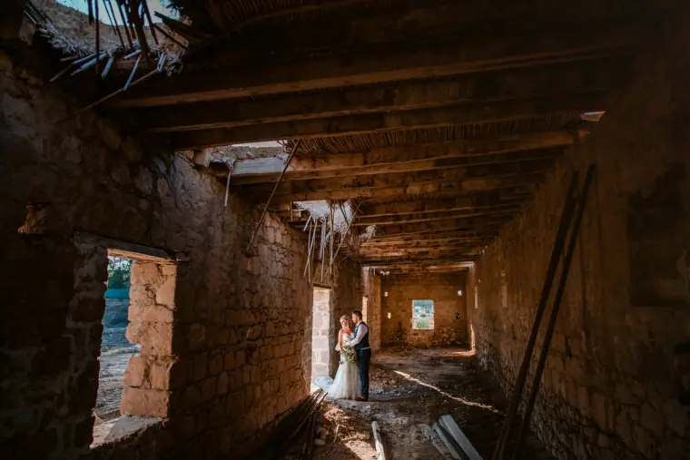Couple standing at the end of a derelict stone barn with a broken roof