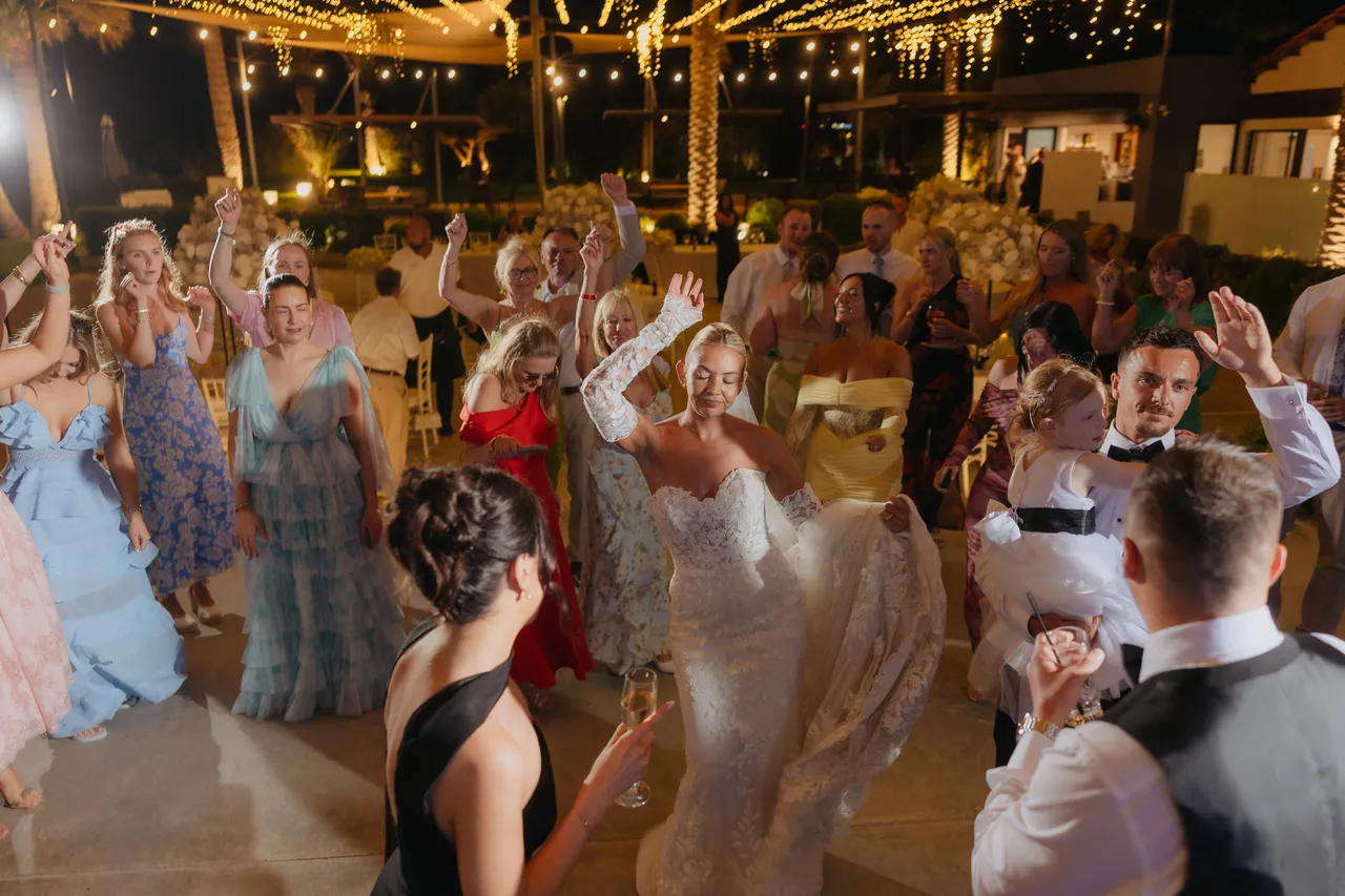 Crowd of guests dancing with the bride beneath string lights