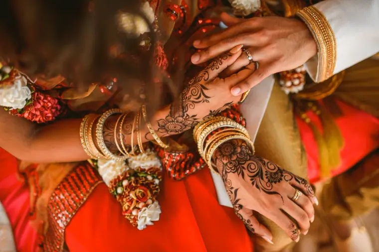 Close-up of the couple's joined hands, the bride's covered in henna and gold bangles
