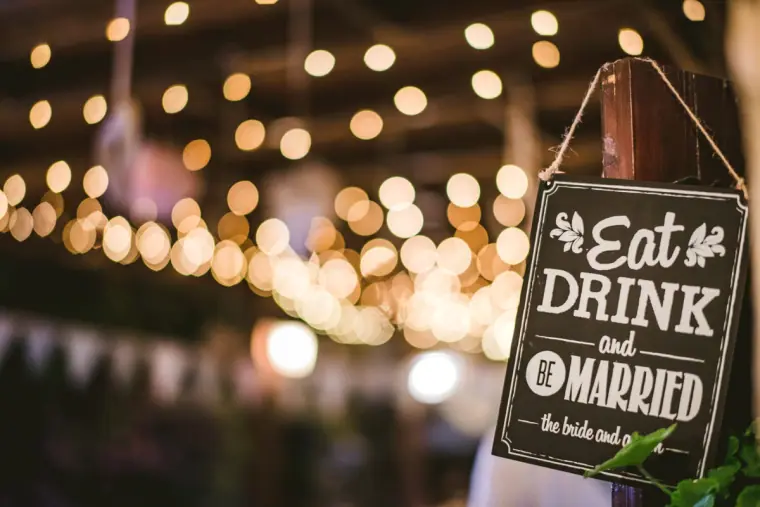 Chalkboard sign reading "Eat, Drink and Be Married" beneath strings of festoon lights
