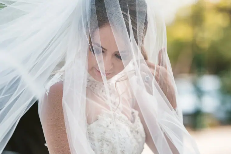 Bride in a beaded bodice looking down through her sheer veil