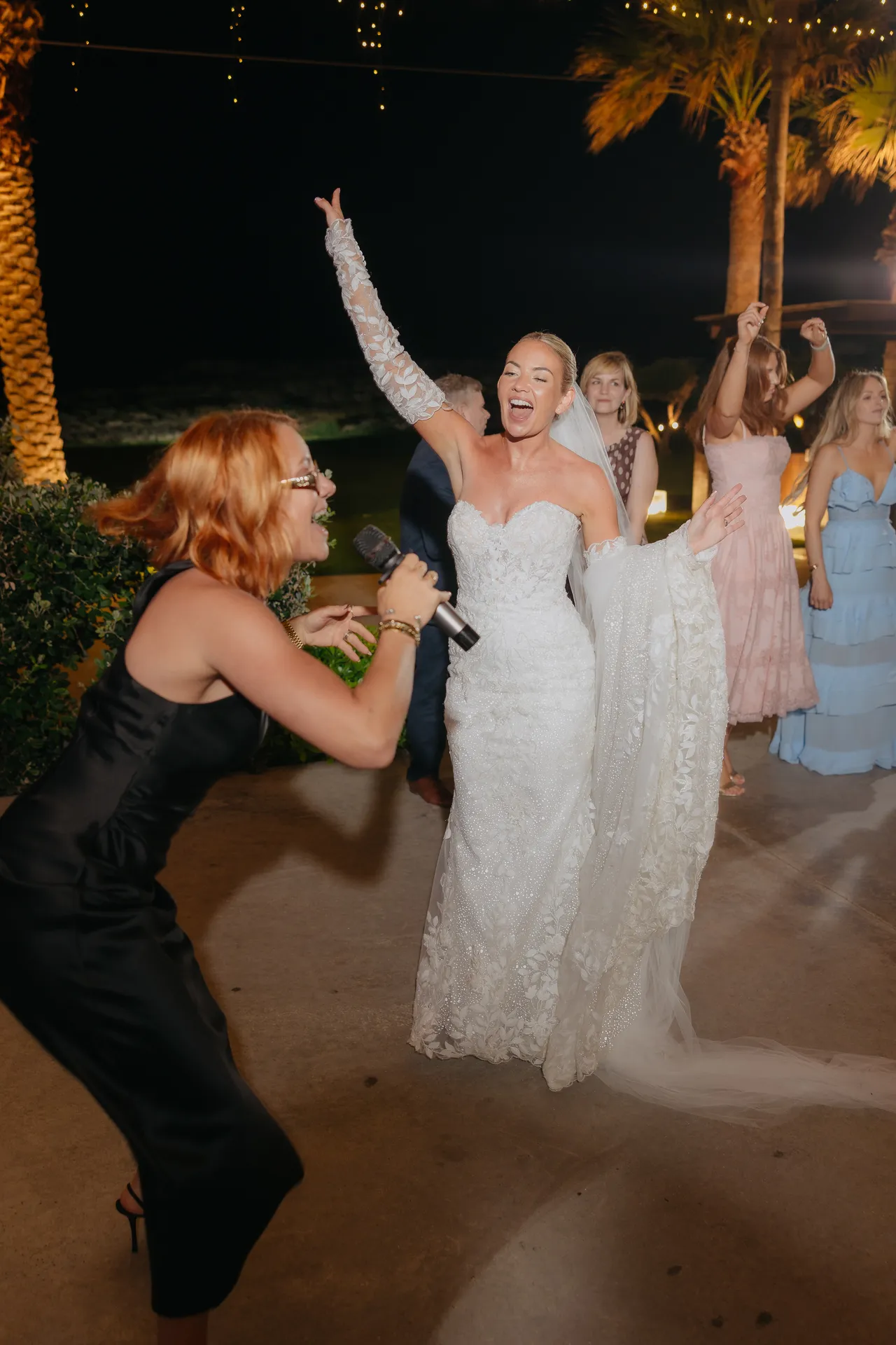 Singer and bride dancing together with arms raised at night