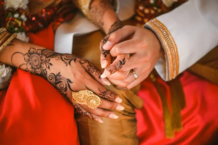 Groom's hand clasping the bride's hennaed hand over her red sari