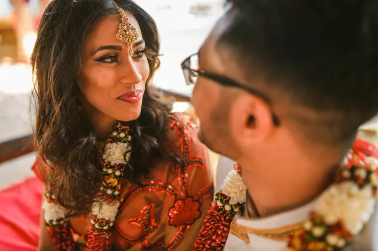 Bride in a maang tikka and garland gazing at the groom