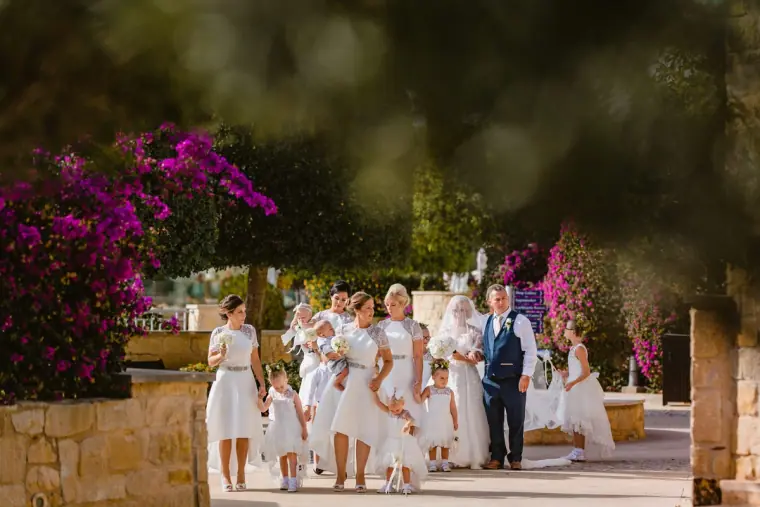 Bridal party in white with flower girls walking past pink bougainvillea
