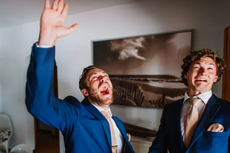 Two groomsmen in suits cheering and laughing during preparations, Can Curreu, Ibiza
