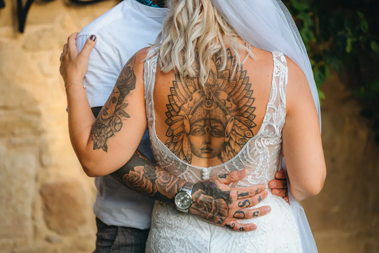 Bride's tattooed back framed by her open-back gown as the groom holds her
