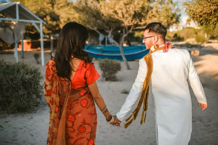 Bride and groom walking hand in hand towards the beach, seen from behind